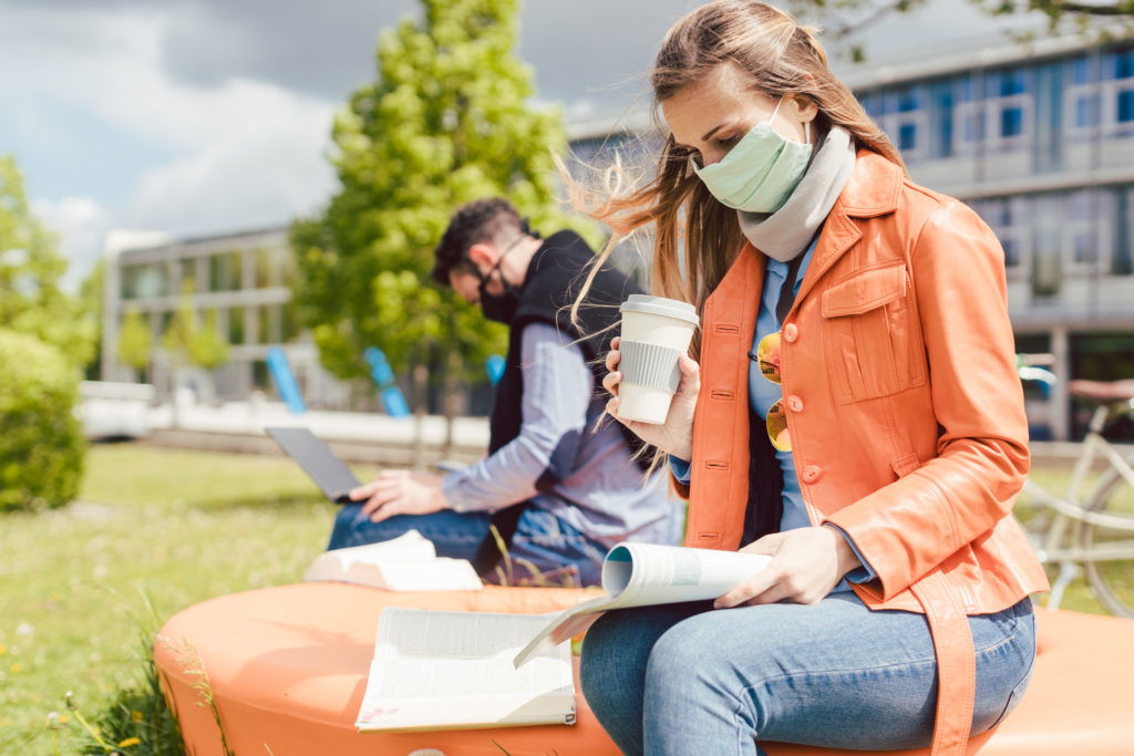 Woman student on college campus learning wearing face mask Woman student on college campus learning wearing face mask while working on her laptop