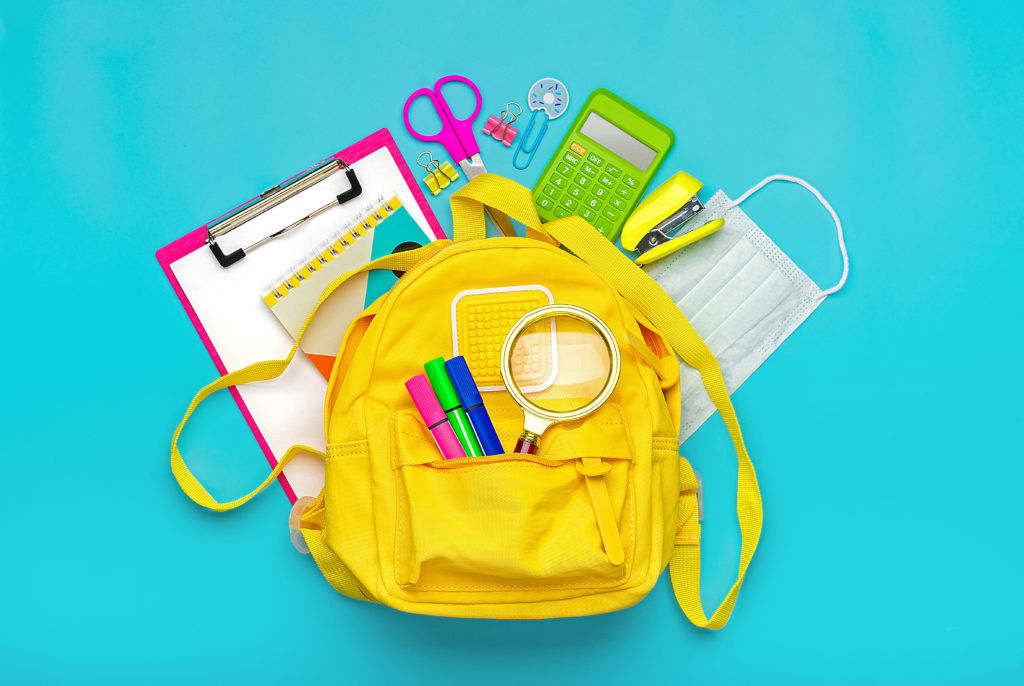Back to school, education concept Yellow backpack with school supplies, protective medical mask, calculator, scissors isolated on blue background. Top view Copy space Flat lay Back to school, education concept Yellow backpack with school supplies, protective medical mask, calculator, scissors isolated on blue background. Top view Copy space Flat lay.
