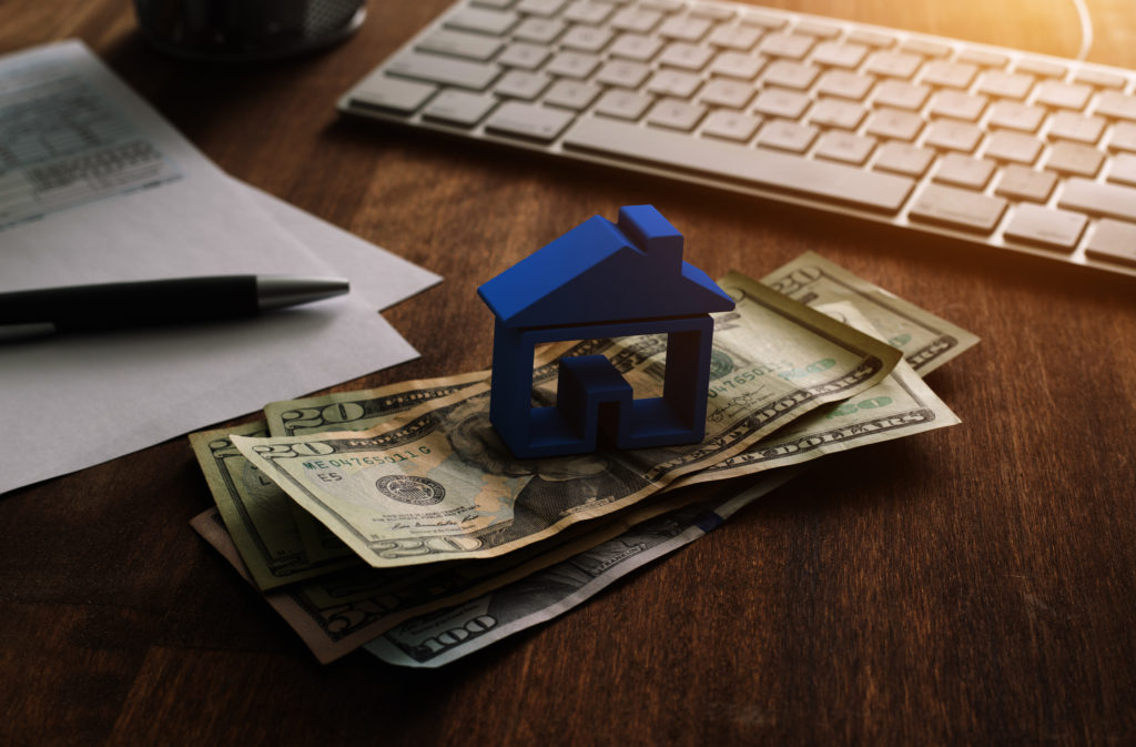 Home Finance Mortgage and Taxes Deduction 3D house on pile of money with tax and financial forms on the desk.