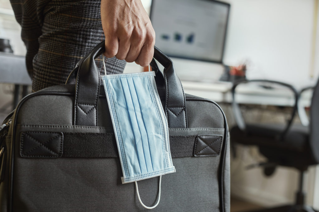 man with a briefcase and a surgical mask closeup of a young man in an office holding a briefcase and a surgical mask in his hand