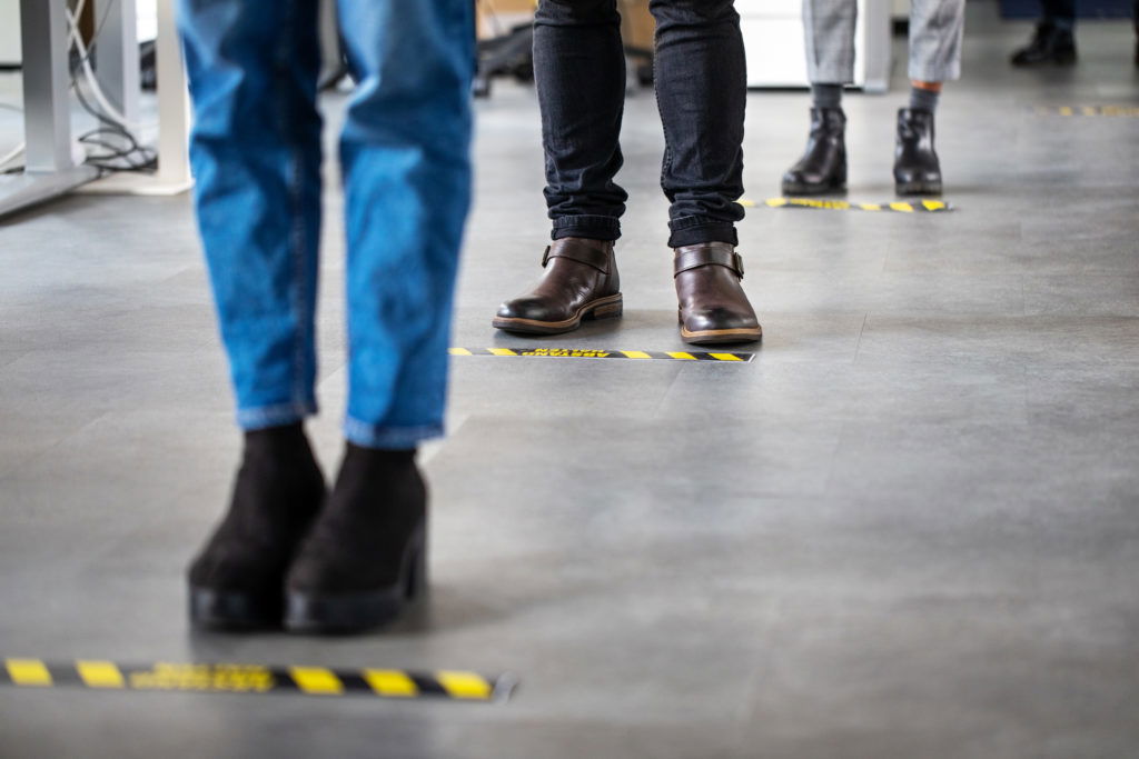 Business people standing behind social distancing signage on office floor Low angle shot of business people standing behind social distancing signage on office floor. People in queue at office for safe entry checks post corona virus pandemic.