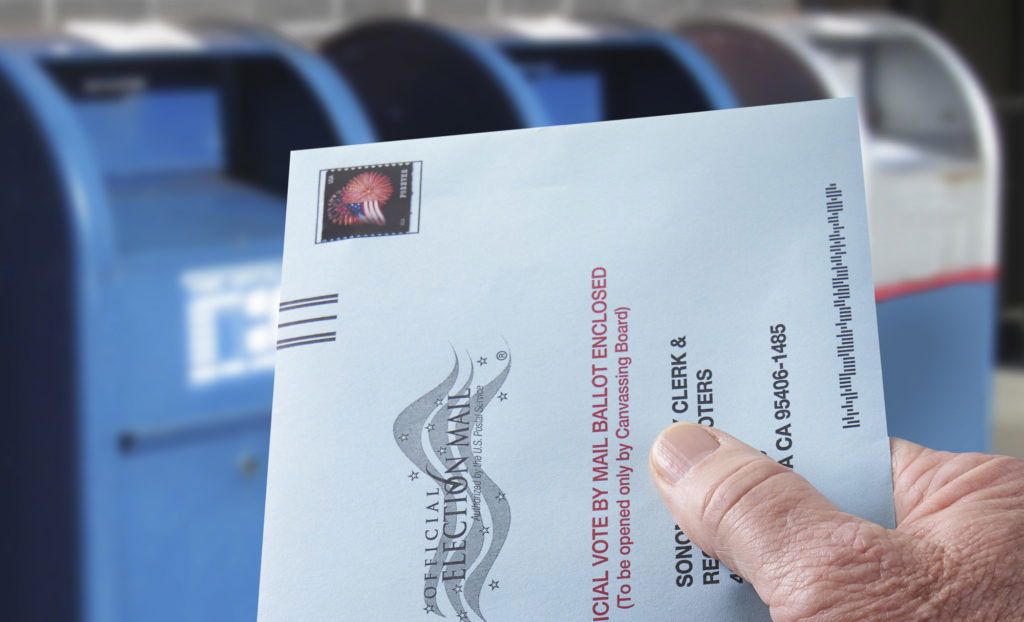 Voting ballot: Absentee voting by mail with hand holding envelope by mailboxes THE SEA RANCH, CALIFORNIA - October 21, 2018: Voting ballot: Absentee voting by mail with hand holding envelope by mailboxes. Absentee voting is voting-by-mail and allows voters who cannot visit the polls on Election Day, to cast their ballot by the US mail.