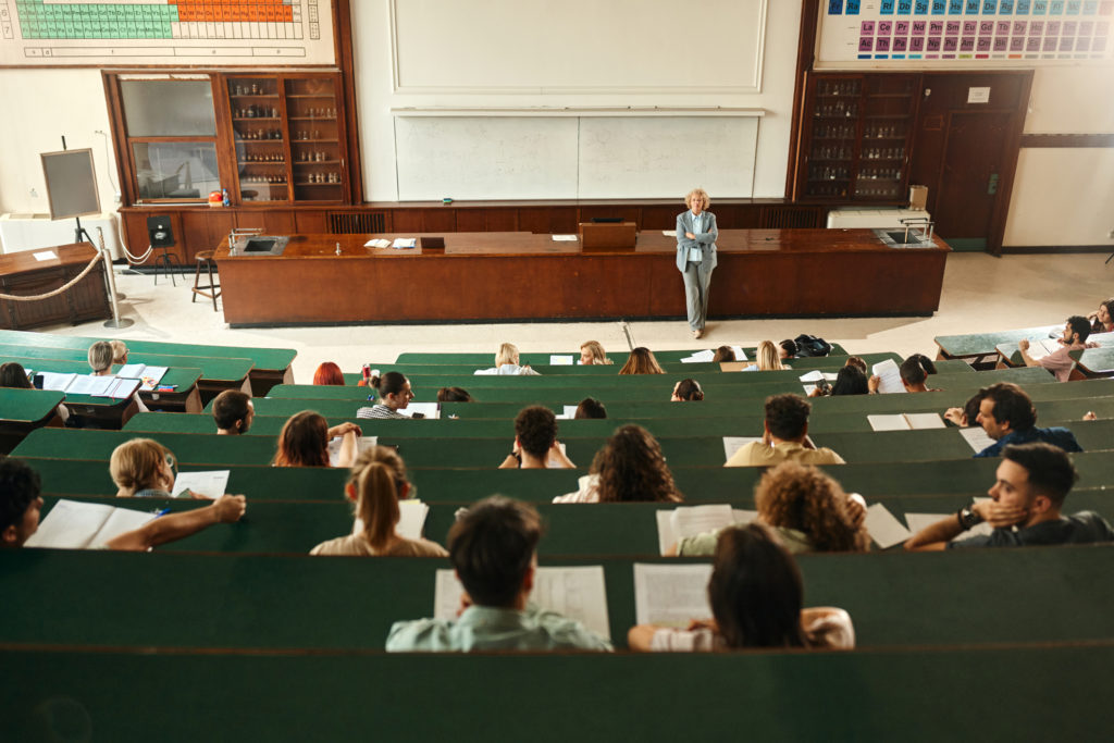 Mature female professor having a class in front of large group of her students at lecture hall. Copy space.
